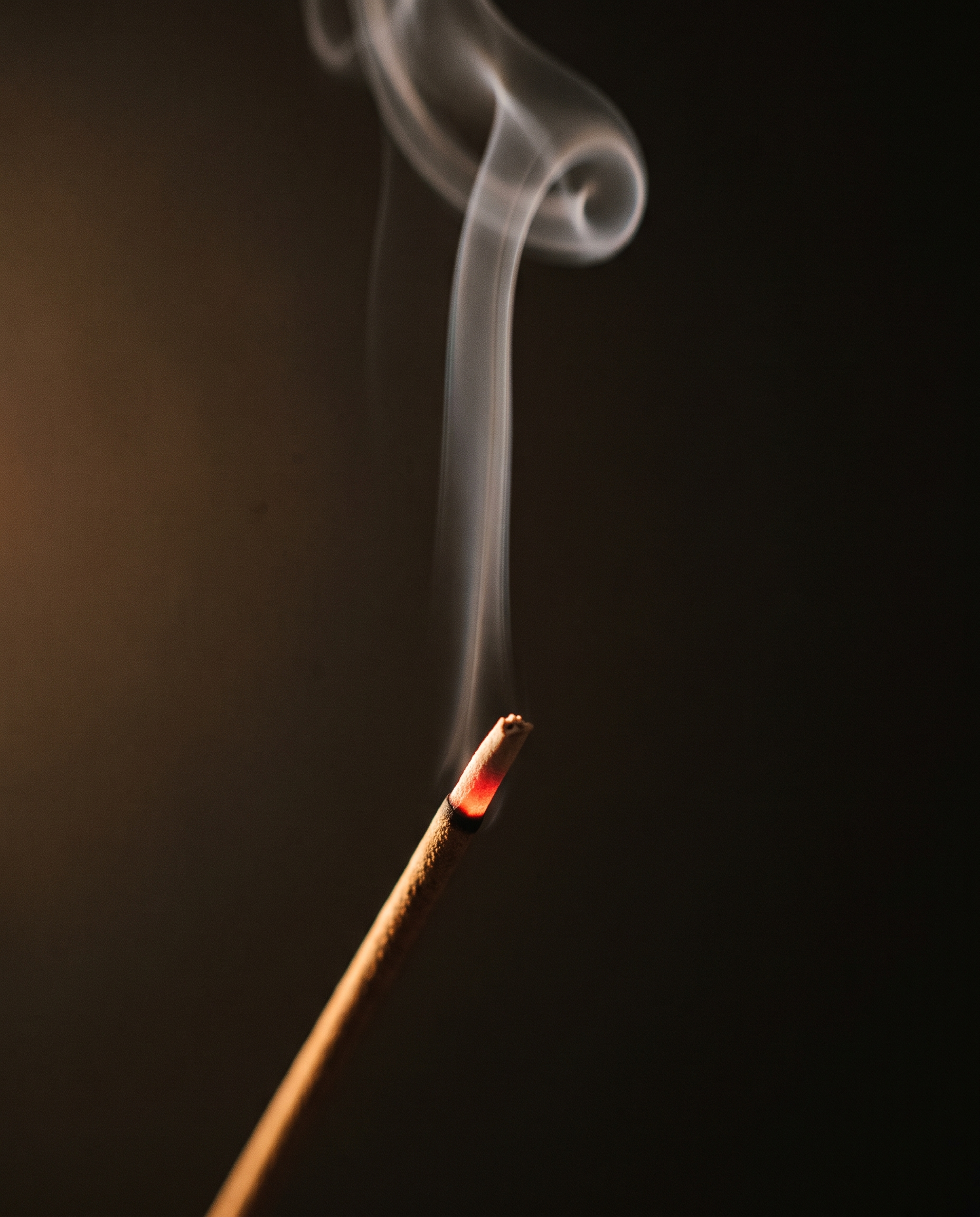 A lit SEN incense stick, ember glowing, a thread of smoke rising